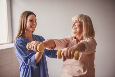 smiling female caregiver and her old woman patient doing exercise