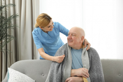 female caregiver giving blanket to her old man patient sitting on the couch